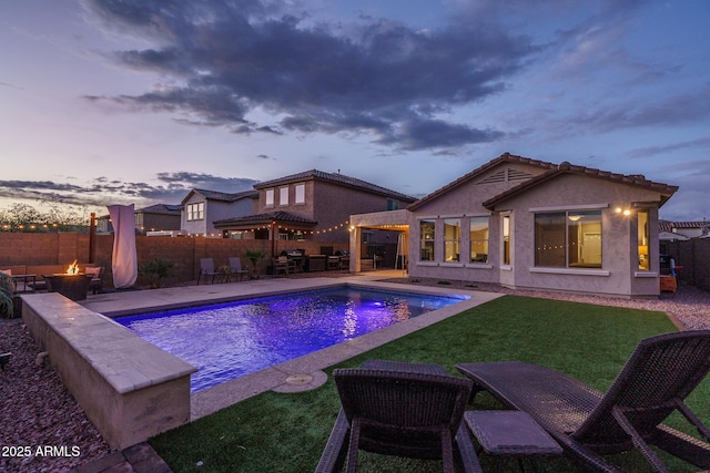 pool at dusk with a fenced in pool, an outdoor fire pit, a lawn, a fenced backyard, and a patio