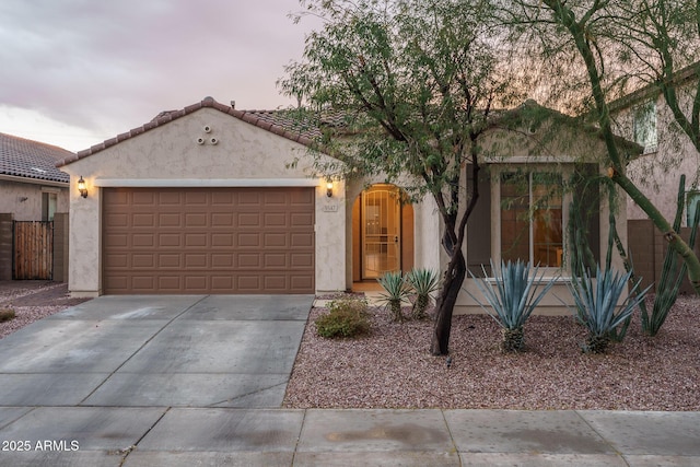 view of front facade with a tiled roof, a garage, driveway, and stucco siding