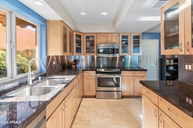 kitchen featuring appliances with stainless steel finishes, light brown cabinets, dark stone counters, and sink