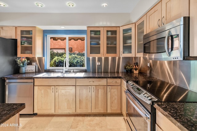 kitchen with sink, dark stone counters, decorative backsplash, light brown cabinetry, and appliances with stainless steel finishes