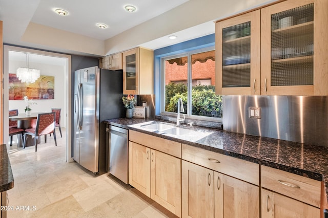 kitchen featuring light brown cabinets, dark stone counters, sink, stainless steel appliances, and a chandelier