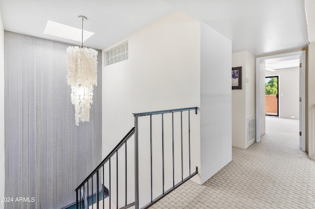 hall featuring light carpet and a chandelier