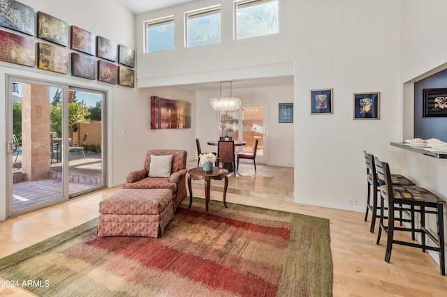 living area with plenty of natural light, light hardwood / wood-style floors, a high ceiling, and an inviting chandelier