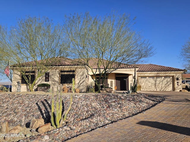 view of front facade featuring decorative driveway, a tiled roof, an attached garage, and stucco siding