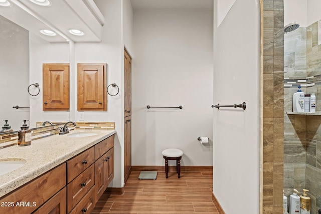 full bathroom with wood finish floors, baseboards, walk in shower, double vanity, and a sink