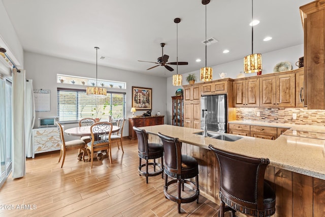 kitchen featuring light stone counters, visible vents, light wood-type flooring, stainless steel fridge with ice dispenser, and tasteful backsplash