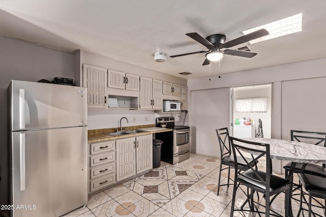 kitchen featuring stainless steel appliances, a sink, a ceiling fan, light tile patterned flooring, and light countertops