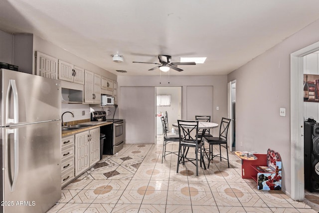 kitchen featuring appliances with stainless steel finishes, a sink, a ceiling fan, light tile patterned floors, and light countertops