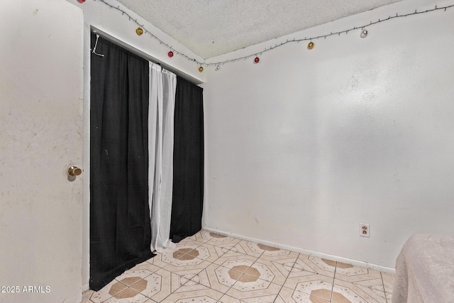 unfurnished room featuring a textured ceiling, light tile patterned flooring, and baseboards