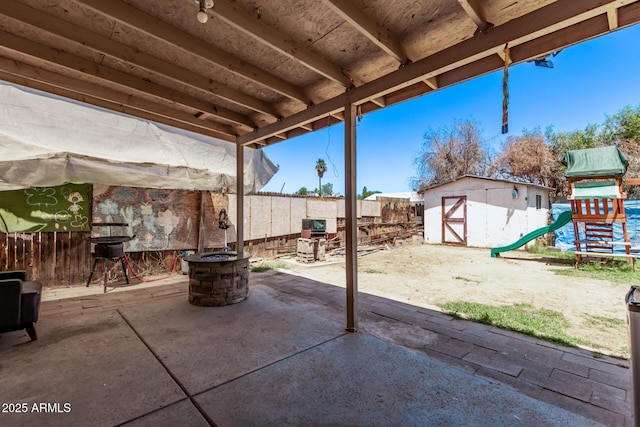 view of patio featuring a shed, a fenced backyard, an outdoor structure, and a playground