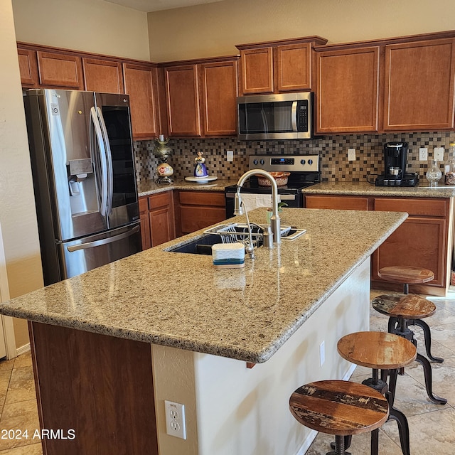 kitchen featuring a breakfast bar, appliances with stainless steel finishes, backsplash, and an island with sink