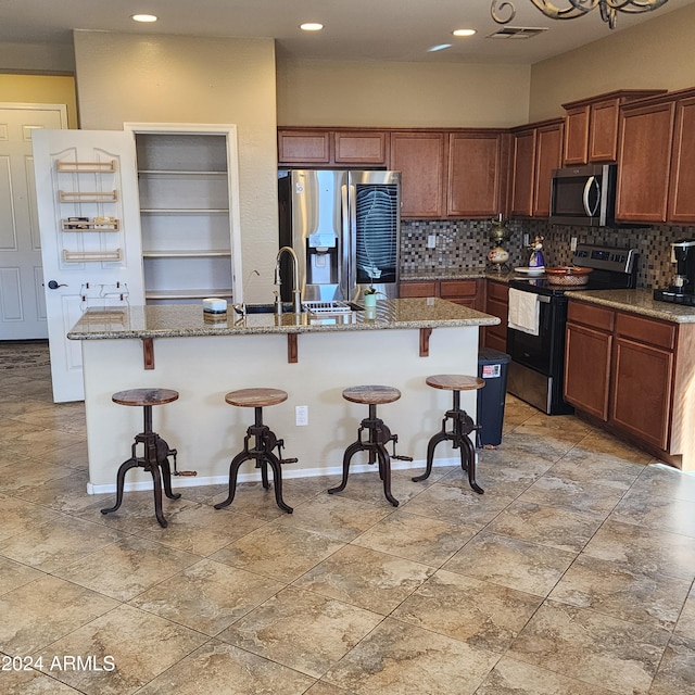 kitchen featuring a breakfast bar, appliances with stainless steel finishes, backsplash, and a center island with sink