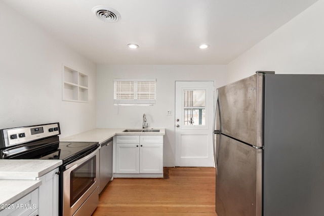 kitchen with visible vents, a sink, white cabinetry, stainless steel appliances, and light wood-style floors