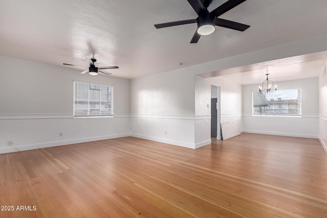 unfurnished living room with ceiling fan with notable chandelier, light wood-style floors, and baseboards