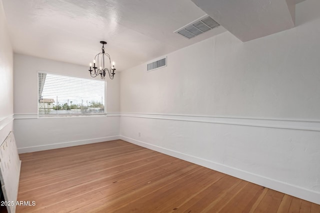 spare room with a notable chandelier, light wood-style floors, and visible vents