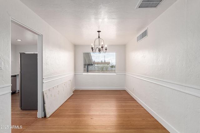 unfurnished dining area with visible vents, light wood-type flooring, an inviting chandelier, and a textured wall