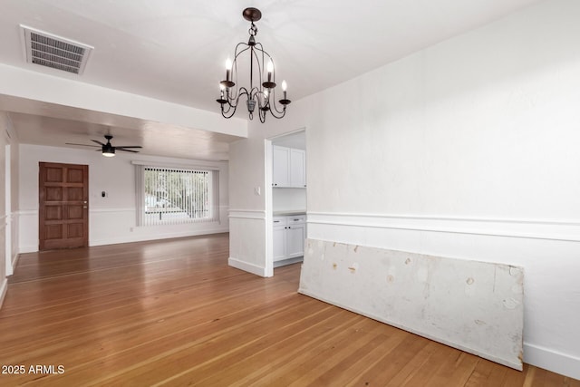 empty room with ceiling fan with notable chandelier, visible vents, light wood finished floors, and baseboards