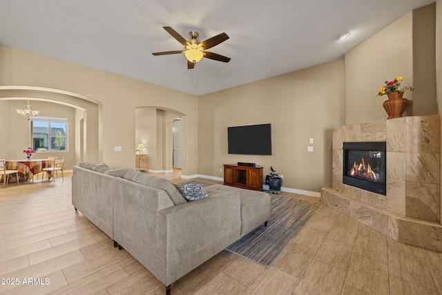 living room with baseboards, arched walkways, ceiling fan with notable chandelier, and a fireplace