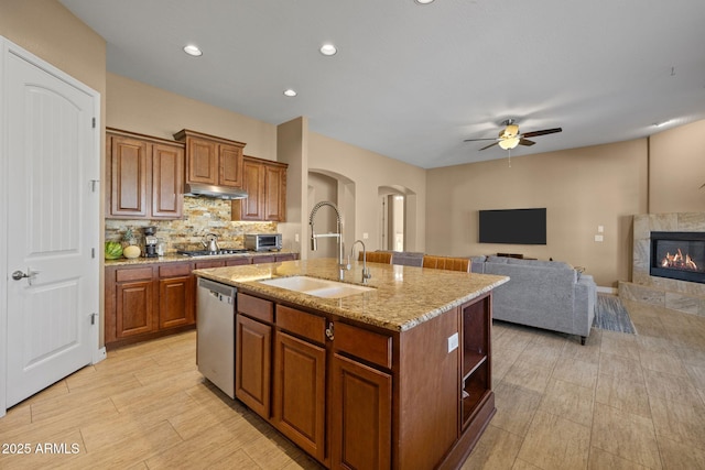 kitchen with stainless steel dishwasher, a ceiling fan, a fireplace, arched walkways, and a sink
