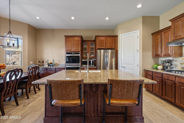 kitchen with stainless steel appliances, light stone countertops, recessed lighting, and a center island with sink