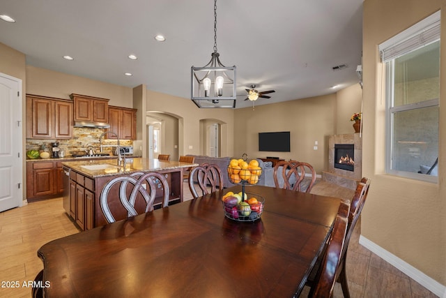 dining room featuring ceiling fan, arched walkways, a tile fireplace, light wood finished floors, and recessed lighting