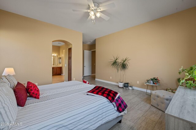 bedroom with connected bathroom, light wood-style floors, arched walkways, a ceiling fan, and baseboards