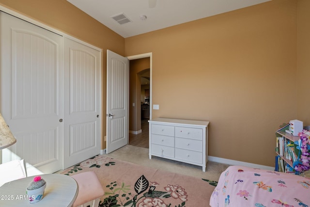 bedroom with a ceiling fan, light colored carpet, visible vents, baseboards, and a closet