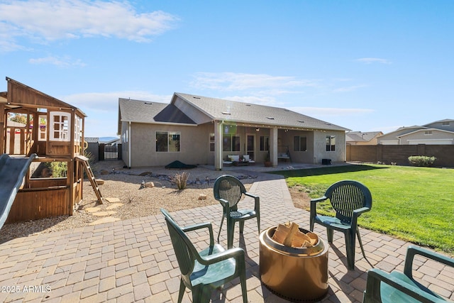 rear view of property with a fenced backyard, a patio area, a playground, a yard, and a fire pit