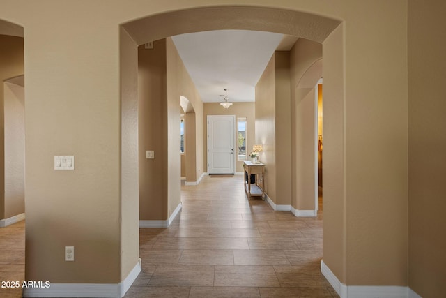 hallway with arched walkways, baseboards, and wood finished floors