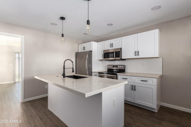 kitchen featuring a kitchen island with sink, hanging light fixtures, sink, light stone counters, and stainless steel appliances