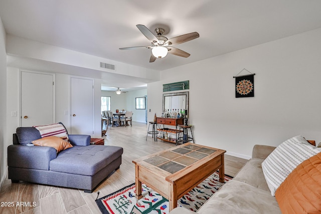 living area featuring baseboards, light wood-style flooring, visible vents, and a ceiling fan