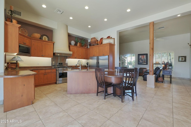 kitchen featuring a kitchen bar, built in appliances, an island with sink, sink, and premium range hood