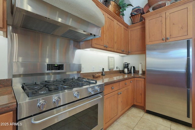 kitchen featuring light tile patterned floors, stainless steel appliances, wall chimney exhaust hood, and dark stone countertops