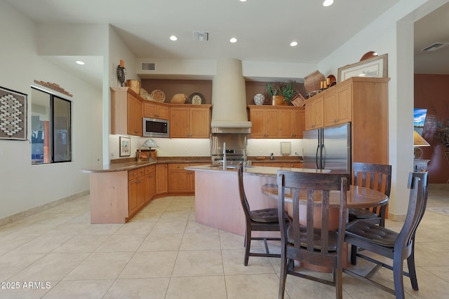 kitchen with appliances with stainless steel finishes, a kitchen bar, kitchen peninsula, light tile patterned flooring, and custom range hood