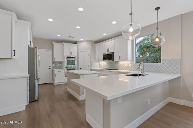 kitchen with a sink, stainless steel appliances, a peninsula, and wood finished floors