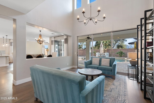 living area with baseboards, a high ceiling, wood finished floors, and ceiling fan with notable chandelier