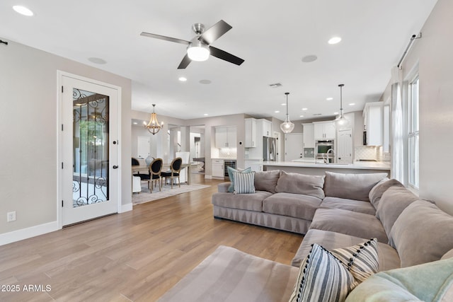 living area with recessed lighting, light wood-type flooring, baseboards, and ceiling fan with notable chandelier