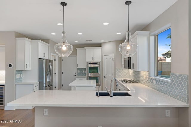 kitchen with wood finished floors, a peninsula, a sink, white cabinets, and appliances with stainless steel finishes