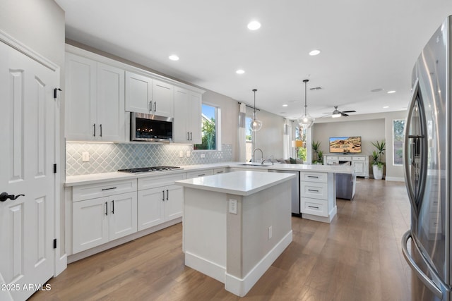 kitchen featuring a center island, light wood-style flooring, appliances with stainless steel finishes, a peninsula, and a sink