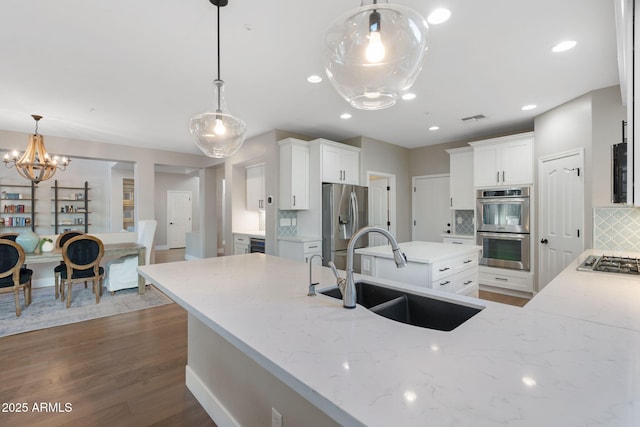 kitchen with visible vents, a sink, backsplash, appliances with stainless steel finishes, and light stone countertops