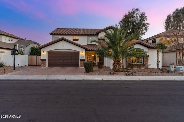 mediterranean / spanish house with stone siding, decorative driveway, a garage, and fence