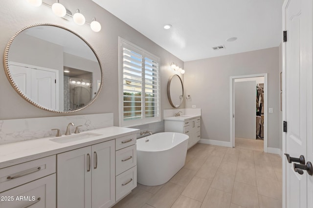 full bathroom featuring visible vents, two vanities, a sink, baseboards, and a soaking tub