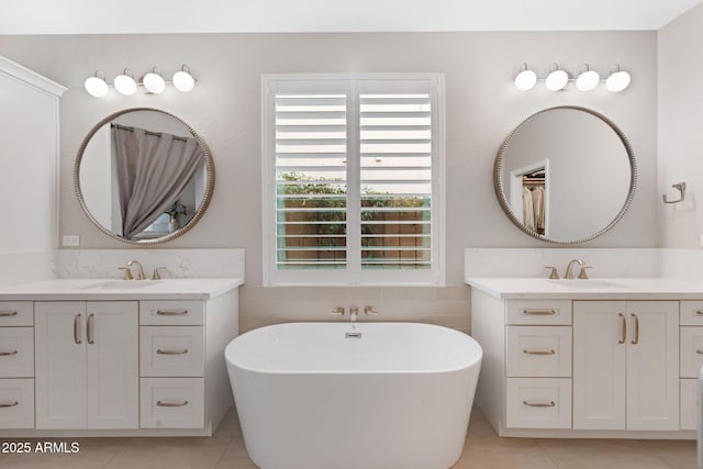 bathroom featuring tile patterned flooring, a freestanding bath, two vanities, and a sink