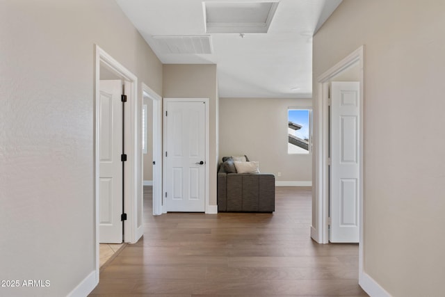 hallway with wood finished floors, visible vents, and baseboards