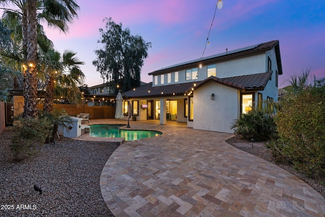 back of property at dusk featuring stucco siding, roof mounted solar panels, a fenced backyard, a fenced in pool, and a patio area