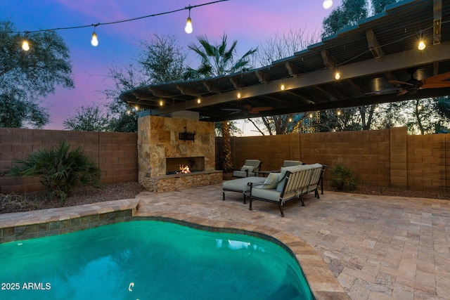 view of swimming pool featuring ceiling fan, a patio, an outdoor stone fireplace, and a fenced backyard