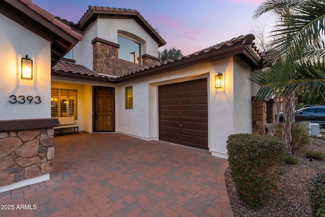 view of front of house with an attached garage, stucco siding, stone siding, a tile roof, and decorative driveway