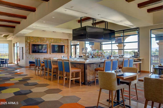 bar with baseboards, beamed ceiling, a community bar, recessed lighting, and wood finished floors