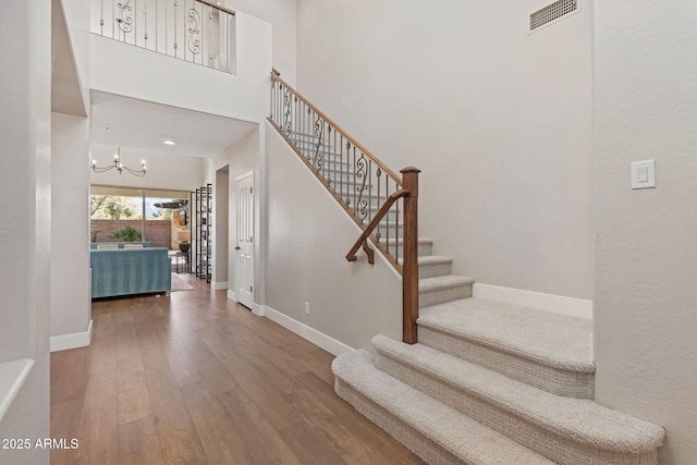 stairs featuring visible vents, wood finished floors, a chandelier, baseboards, and a towering ceiling