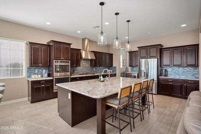 kitchen featuring tasteful backsplash, dark brown cabinetry, stainless steel appliances, wall chimney range hood, and visible vents